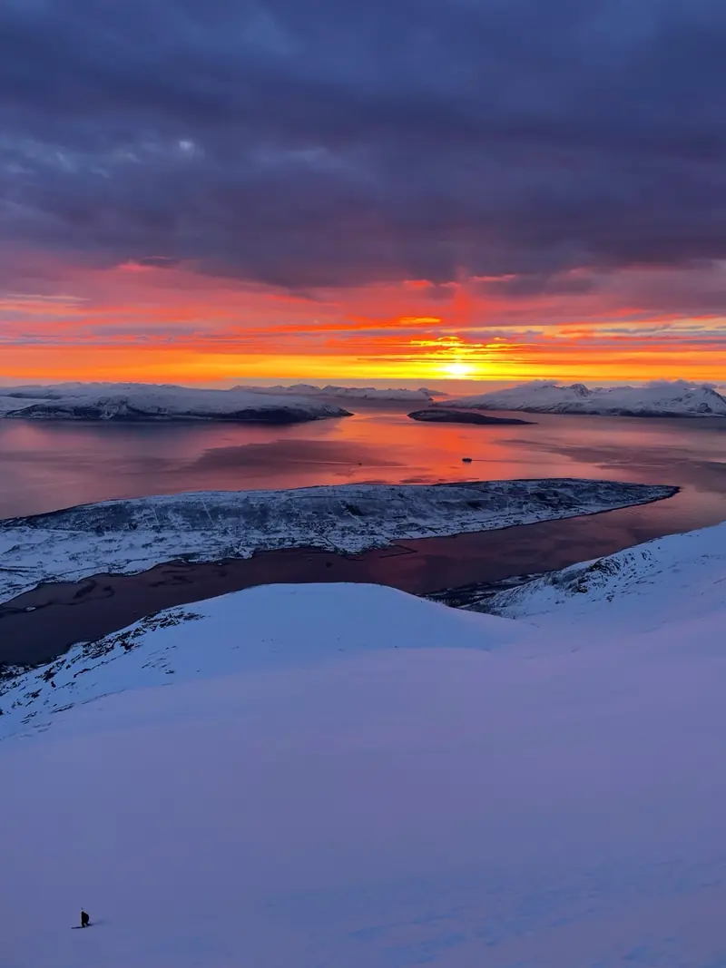 Nuages incandescents au coucher du soleil au-dessus de l'eau et de collines enneigées