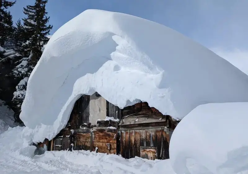 Une cabane en bois sous un énorme coussin de neige