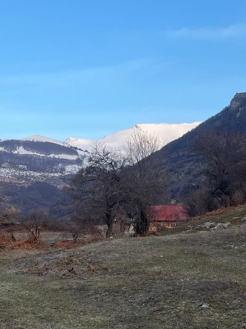 Eine Hütte mit rotem Dach in einem Bergtal unter einem verschneiten Gipfel