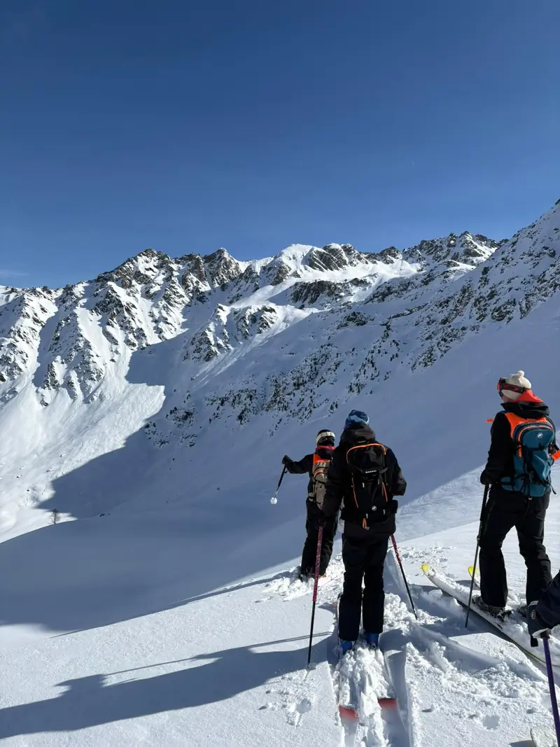 Three skiers on a ridge looking toward steep rocky peaks