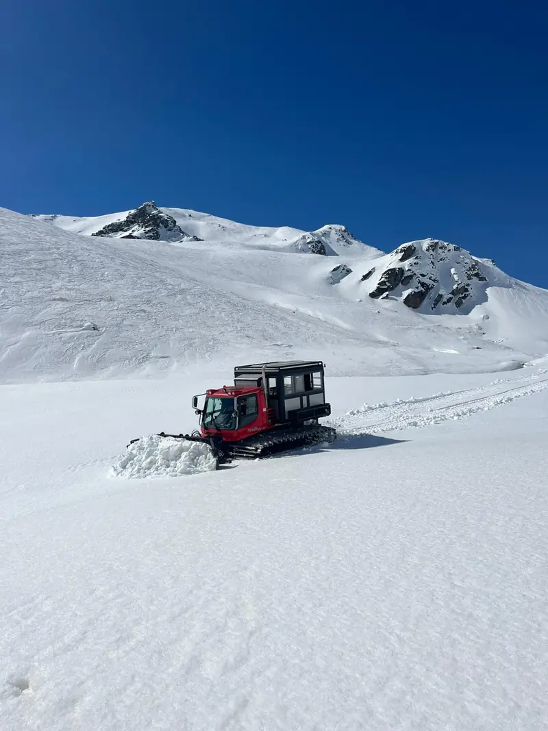 Le snowcat grimpe dans la poudreuse fraîche sous des sommets rocheux
