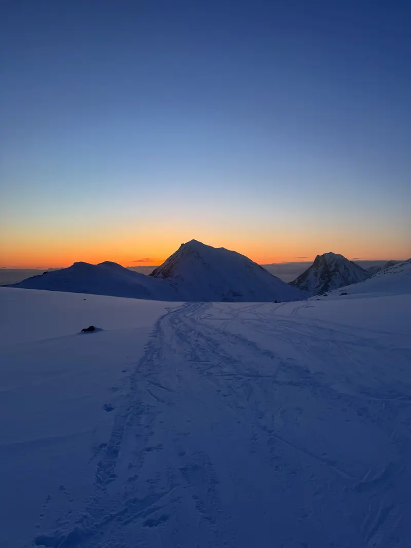 Coucher de soleil derrière un sommet pointu, traces de ski au premier plan