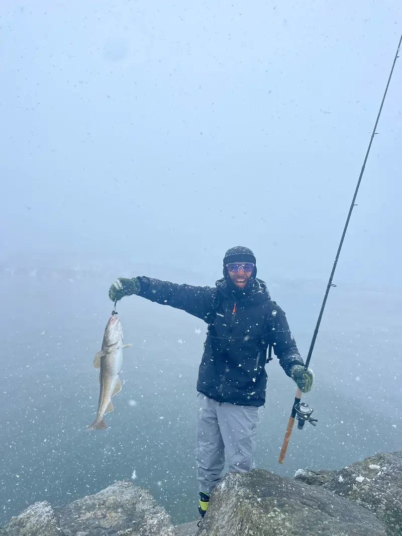 Un skieur brandissant un poisson fraîchement pêché au bord de la mer arctique