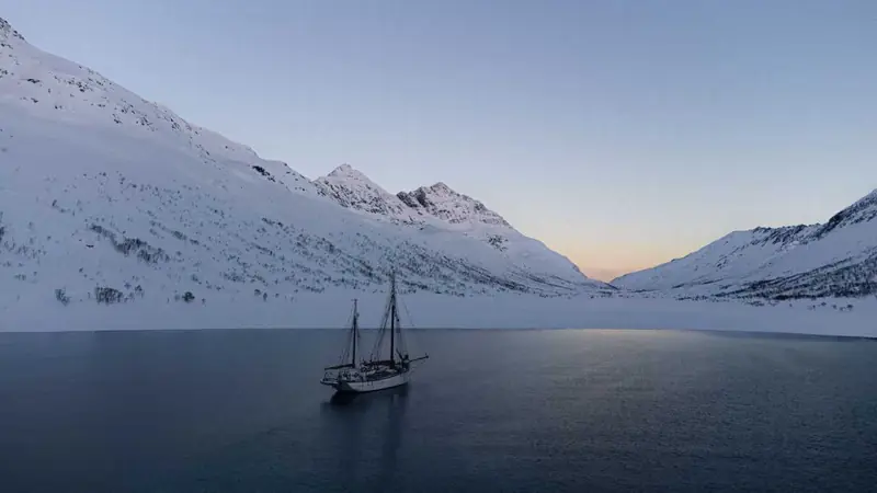 Un voilier au mouillage dans un fjord calme entouré de montagnes enneigées