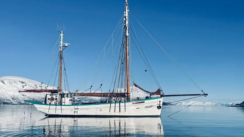 A two-masted schooner on still water beside snow-covered shores
