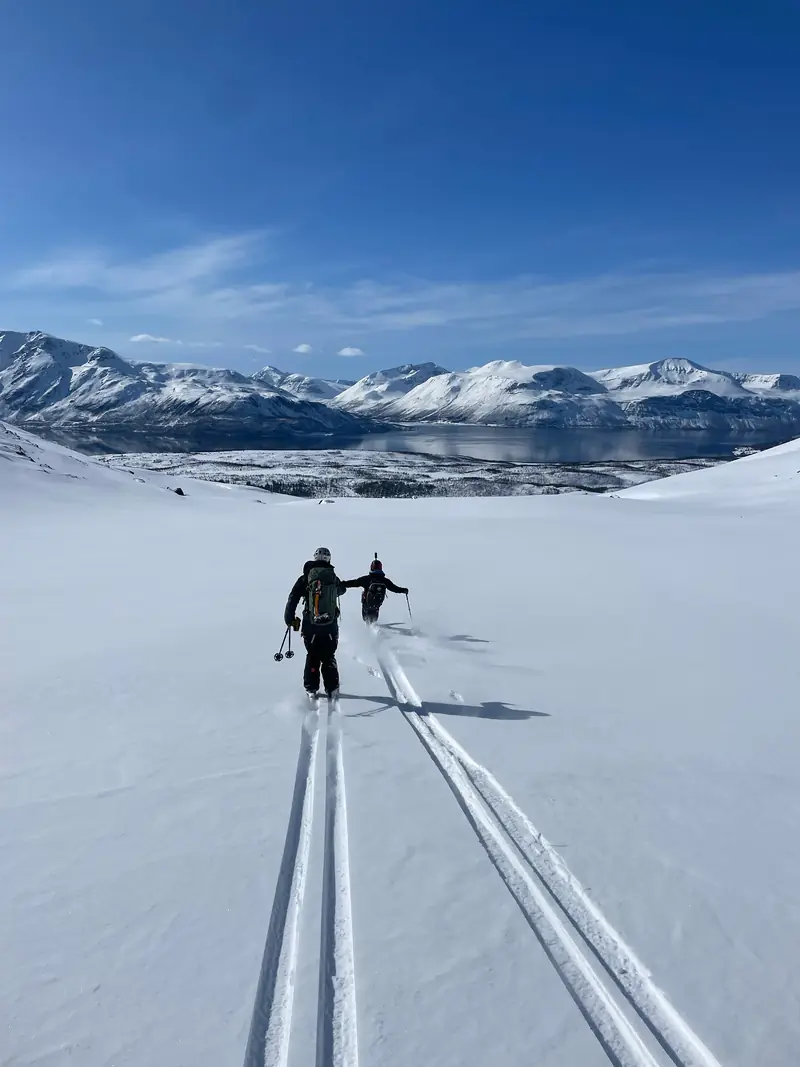 Deux randonneurs à ski suivant une trace vers un fjord et des sommets enneigés