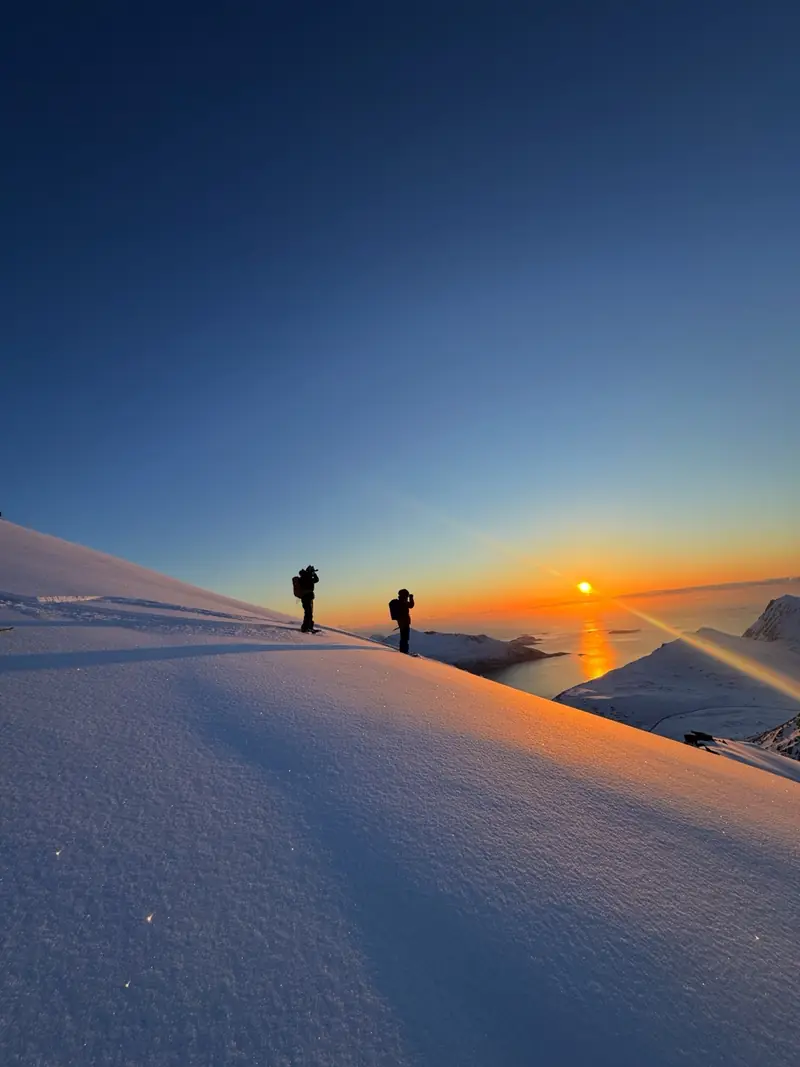 Deux skieurs de randonnée sur une crête face au soleil arctique rasant au-dessus de la mer