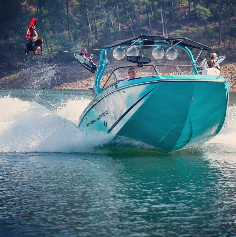 A wake boat carving the lake with a rider behind it