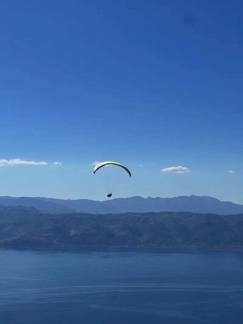 Ein Gleitschirmflieger hoch über einem grossen See und den Bergen